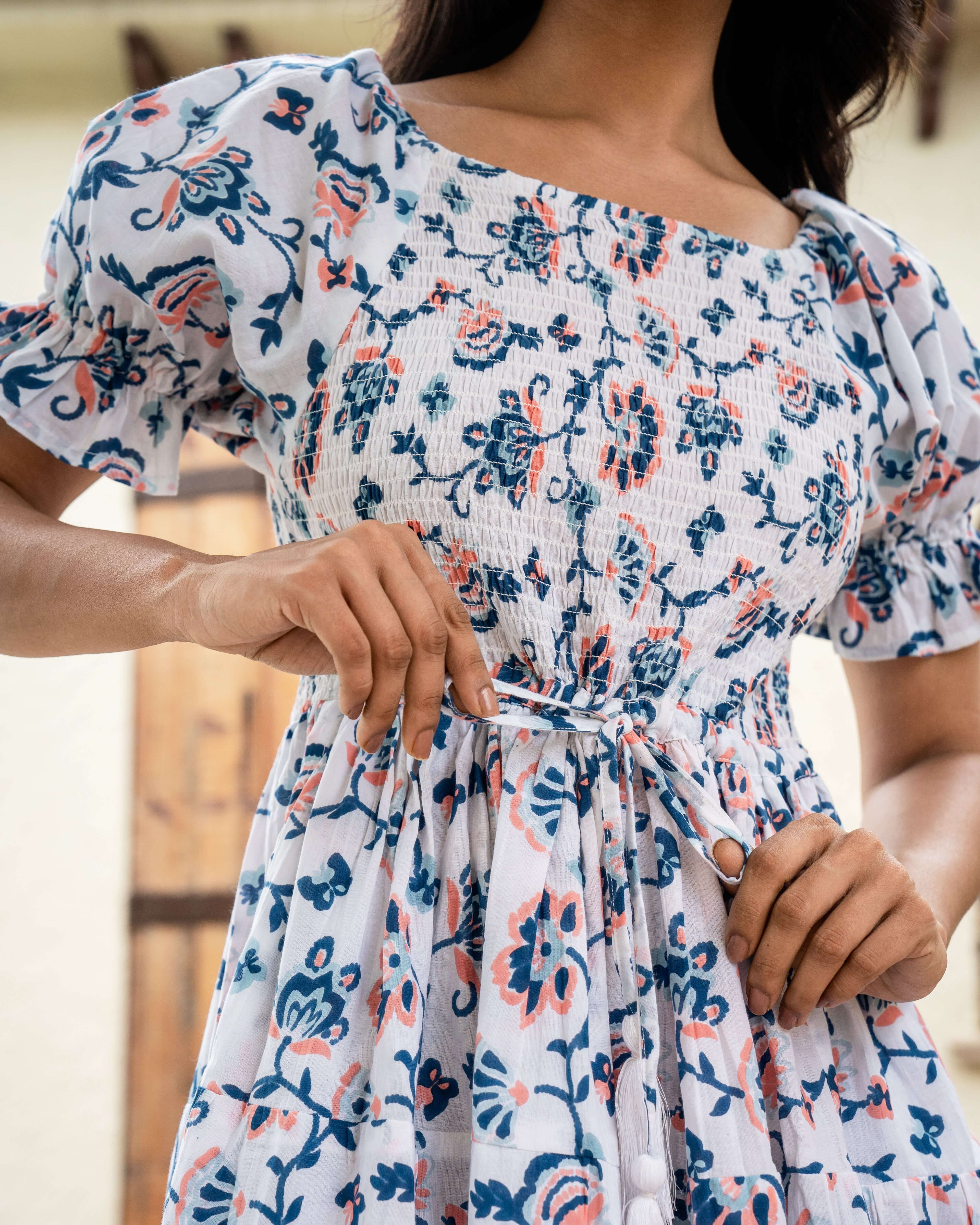 Elegant cotton midi dress in blue and peach floral prints over white, featuring a shirred chest and adjustable sleeves for a customizable fit.