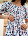 Elegant cotton midi dress in blue and peach floral prints over white, featuring a shirred chest and adjustable sleeves for a customizable fit.